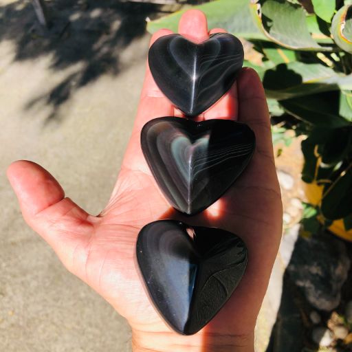 Tres corazones de obsidiana arco iris sobre palma de la mano